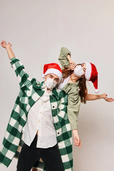 Femme dans un masque médical et un homme dans un chapeau de Noël font un geste avec leurs mains sur un fond clair — Photo