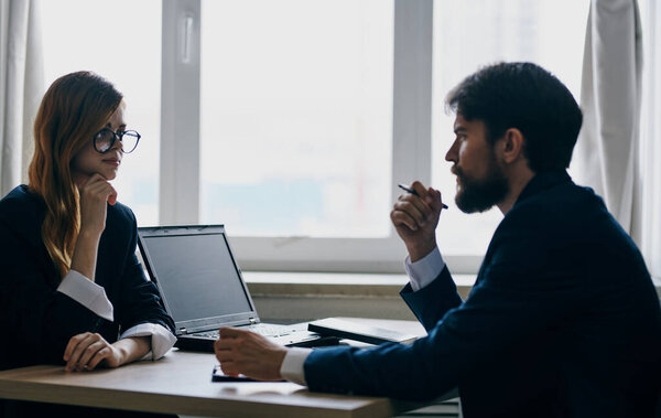 A business man in a suit and a woman communicate at work opposite each other at the table in the office