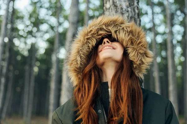 Vrouw met een kap op haar hoofd kijkt op tegen de achtergrond van de herfstboswandeling — Stockfoto