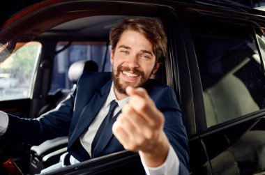 Takım elbiseli mutlu adam arabasının camından dışarı bakar ve elleriyle hareket eder.