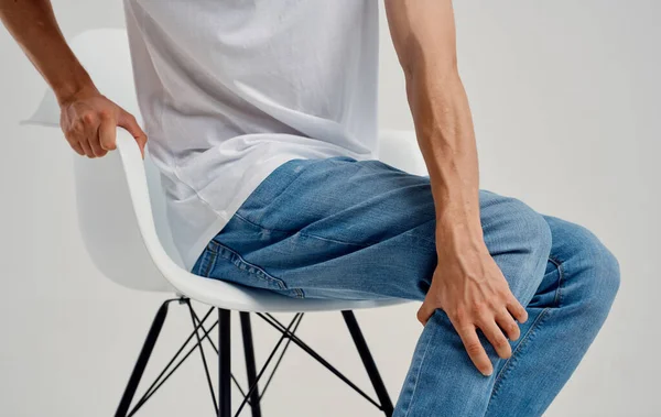 Mann in Jeans sitzt auf einem Stuhl und berührt sein Bein mit abgeschnittenen Händen — Stockfoto