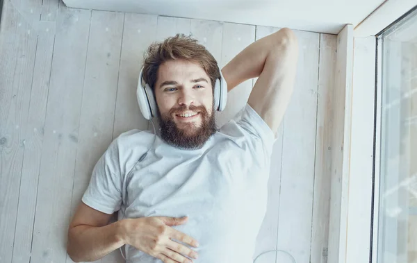 cheerful bearded man lies on the windowsill with headphones music technology