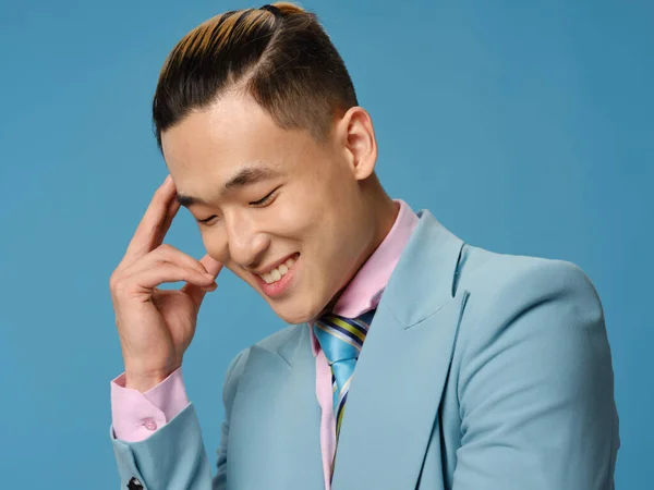 Happy Asian man touching face with hand and smiling on blue background