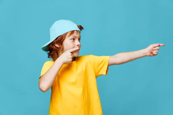 Vörös hajú fiú mutatja az ujját az oldalsó sárga póló kék sapka — Stock Fotó