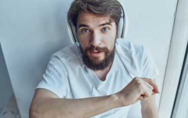 Kulaklık takan sakallı adam, pencerenin yanında dinleniyor.