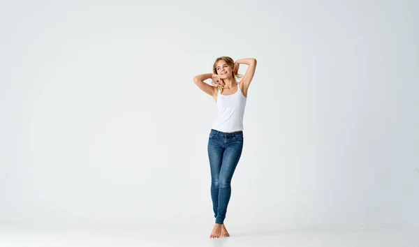 Žena v džínách a bílé tričko na světlém pozadí v plném růstu — Stock fotografie