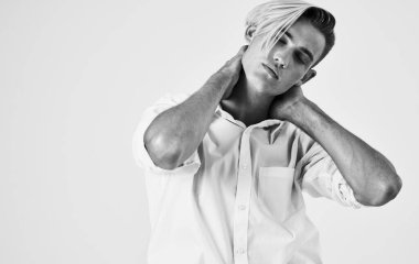 Hafif arka planda pantolon ve gömlek giymiş genç bir adam elleriyle kafasına dokunuyor.