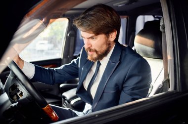 Saldırgan iş adamı arabanın camından dışarı bakıyor ve elleriyle el kol hareketi yapıyor.