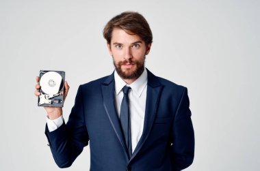 Takım elbiseli bir adam elinde birleştirilmemiş bir sabit disk ve gri bir arka plan tutuyor.