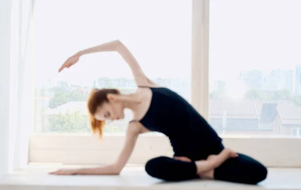 Seorang wanita dalam pakaian gelap duduk berkaki silang di lantai dan gerak tubuh dengan tangannya di yoga asana — Stok Foto