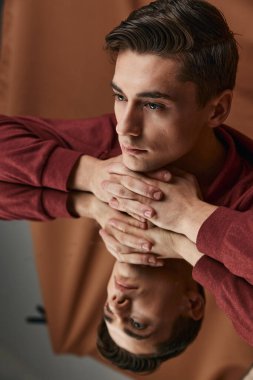 Kahverengi gömlekli adam cama yaslanıyor. Mankenin bir yansıması.