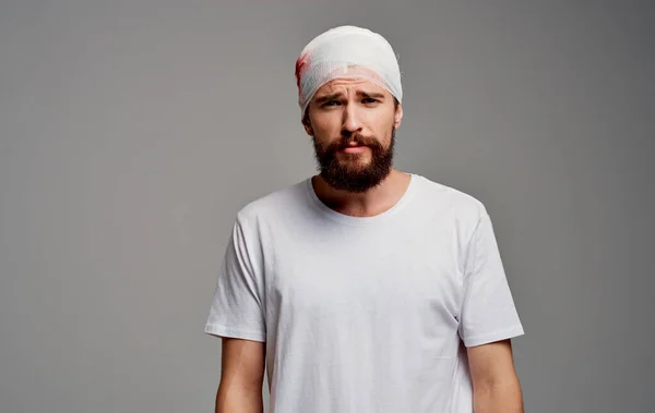 Un hombre con una cabeza vendada sangre en su brazo operación gris fondo blanco camiseta —  Fotos de Stock