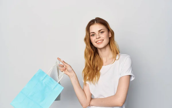 Roztomilé rusovlasá žena v bílém tričku s balíčky v ruce nakupování izolované pozadí. — Stock fotografie