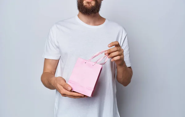 Homem em uma camiseta com um saco de presente rosa em um fundo claro — Fotografia de Stock