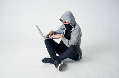 Maskeli bir adam dizüstü bilgisayarın önünde oturup suçu hackliyor.