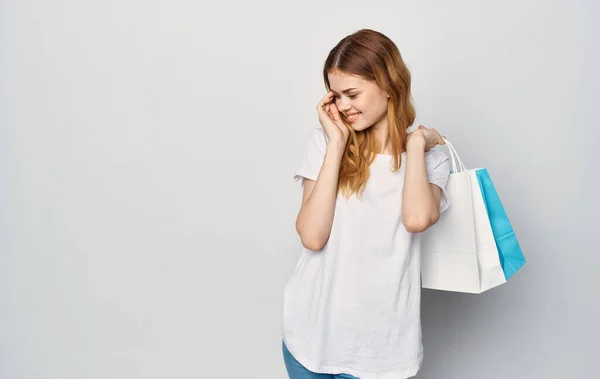 Όμορφη γυναίκα σε ένα λευκό T-shirt με πακέτα στα χέρια ψώνια απομονωμένη φόντο — Φωτογραφία Αρχείου