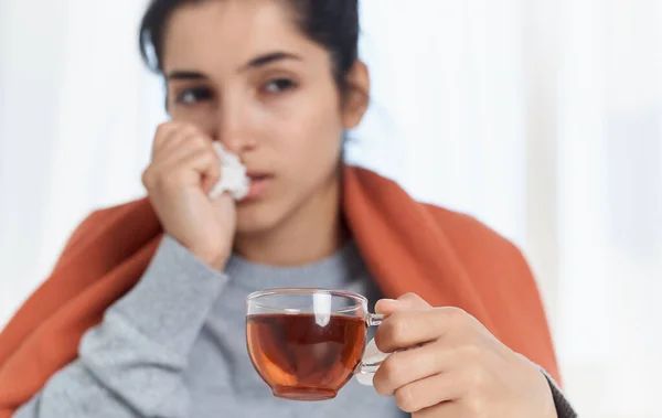 Erkältete Frau im orangefarbenen Karo mit einer Tasse Tee und einer Serviette in der Hand — Stockfoto