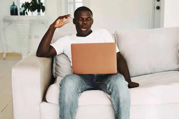 A man at home on the couch with a laptop on his lap African appearance — стокове фото