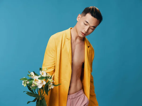Homem com um buquê de flores brancas em um fundo azul amarelo casaco rosa calças torso nu — Fotografia de Stock