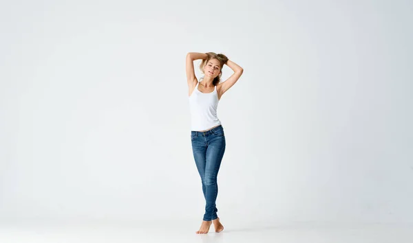 Mujer en jeans y una camiseta blanca sobre un fondo claro en pleno crecimiento —  Fotos de Stock