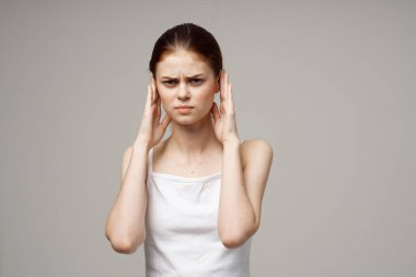 Kulakları olan beyaz tişörtlü kadının migren sorunları var.