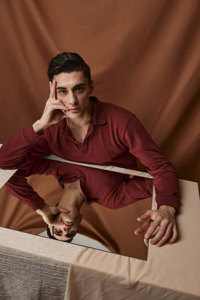 Handsome guy in shirt posing at a table indoors on a fabric background — Stock Photo, Image