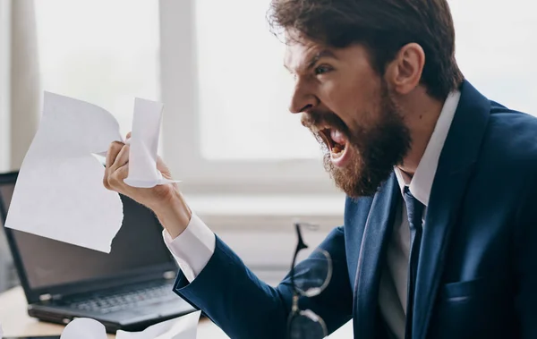 Aggressive business man in a suit with white sheets of paper in his hands in the office near the window