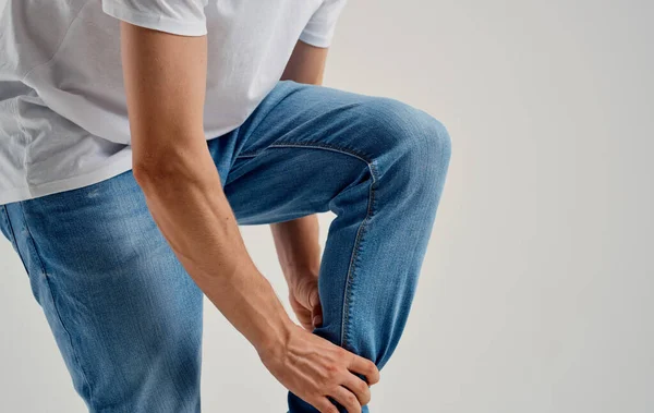 Man in jeans raakt zijn knie met zijn handen op een lichte achtergrond bijgesneden uitzicht — Stockfoto