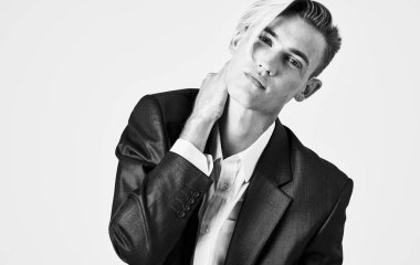 Yakışıklı genç adam elini yüzüne yakın tutuyor açık arka planda bir takım elbise manzarası.