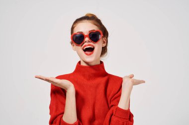 Kırmızı kazaklı ve gözlüklü kadın ellerini kırpmış mekanı kopyalayarak el kol hareketi yapıyor.