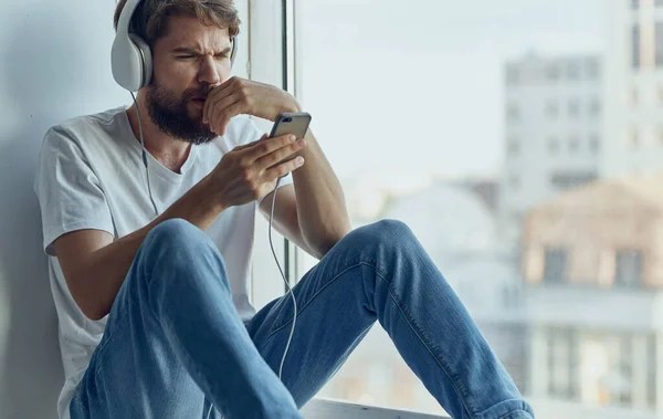 Uomo barbuto in cuffia ascoltare musica vicino alla tecnologia di ricreazione finestra — Foto Stock