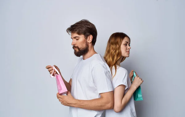 Άνδρας και γυναίκα με τσάντες δώρων στέκονται ο ένας πίσω στον άλλο σε γκρι φόντο — Φωτογραφία Αρχείου