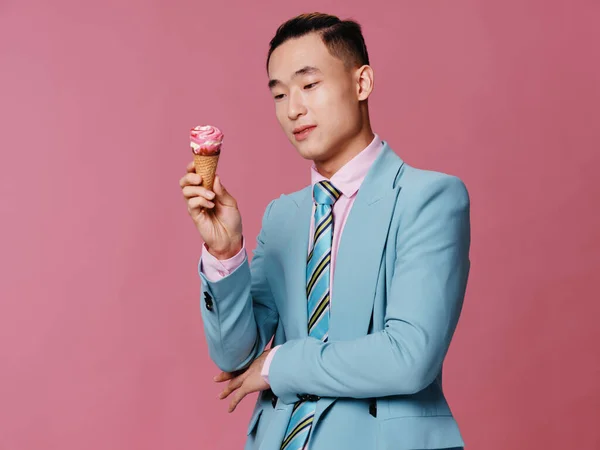 Cute man of Asian appearance in blue suit ice cream in hands on pink background — Stock Photo, Image