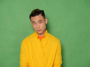 Sarı ceketli yeşil arka planda yakışıklı bir Asyalı.