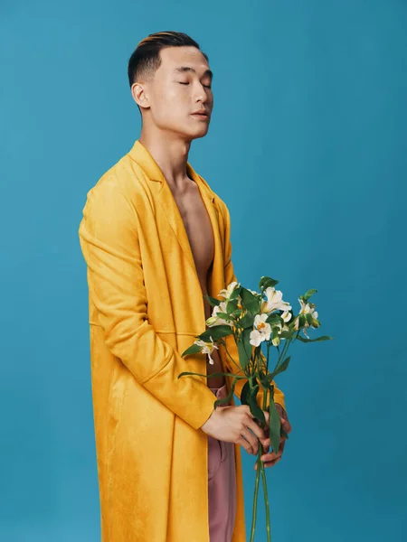 Charmoso homem asiático com um buquê de flores e um casaco amarelo calças rosa torso nu — Fotografia de Stock