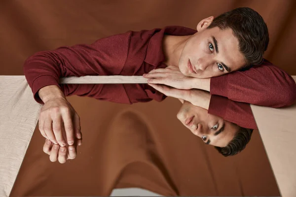 Homem bonito encontra-se em uma mesa com um espelho e tecido modelo de fundo — Fotografia de Stock