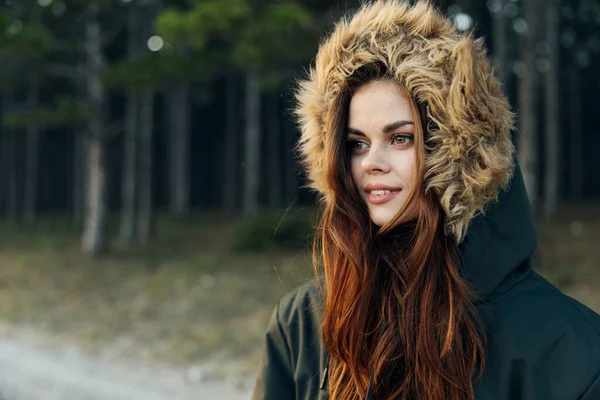 Vrouw in een jas met een kap koele natuur op de achtergrond van bomen — Stockfoto