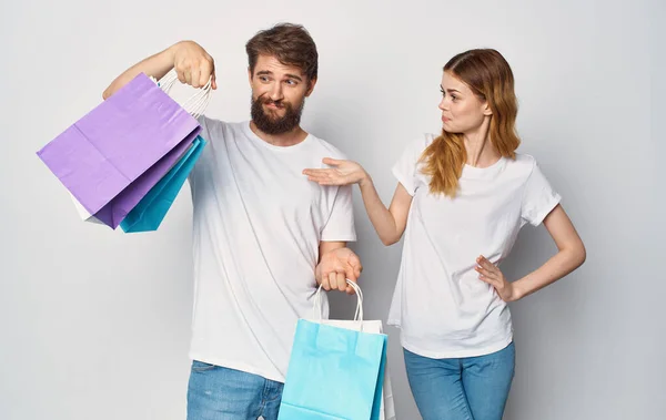 Feliz pareja joven en camisetas blancas con paquetes en las manos Compras es alegría — Foto de Stock