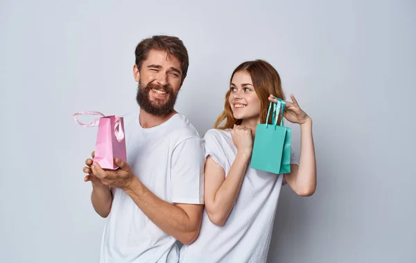 Homem e mulher com sacos de presente ficar de volta uns aos outros em fundo cinza — Fotografia de Stock