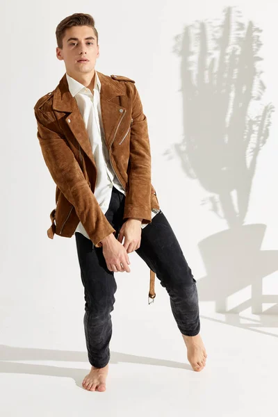 Un hombre guapo en pantalones y una chaqueta marrón está bailando sobre un fondo claro — Foto de Stock