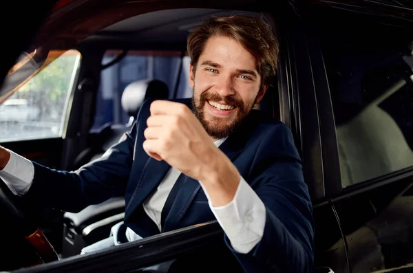 Homem feliz de terno olha para fora da janela do carro e gestos com as mãos — Fotografia de Stock