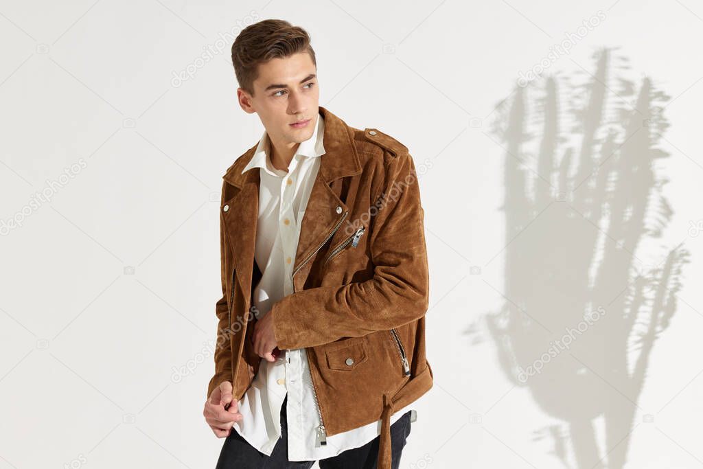 A handsome guy in a brown jacket in a white shirt and a falling shadow from a flower on a light background