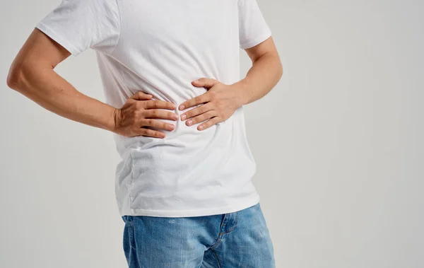 Chico en una camiseta y jeans toca sus manos cerca del dolor abdominal problemas estomacales apendicitis — Foto de Stock