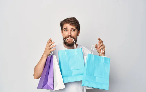 Bärtiger Mann im weißen T-Shirt mit Paketen in der Hand einkaufen Urlaub isoliert Zeichen — Stockfoto