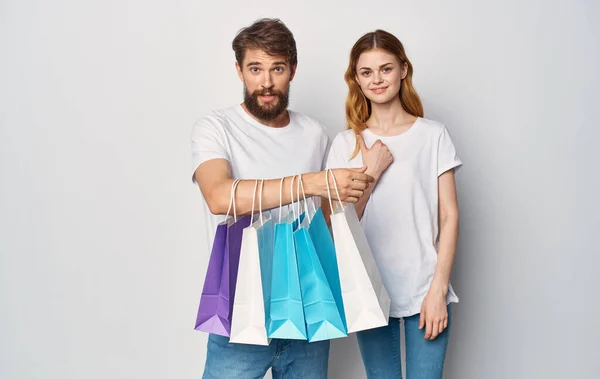 Feliz pareja joven en camisetas blancas con paquetes en las manos Compras es alegría —  Fotos de Stock