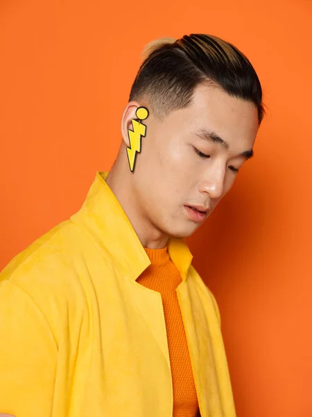 Asian guy with an earring in his ear on an orange background and a yellow jacket