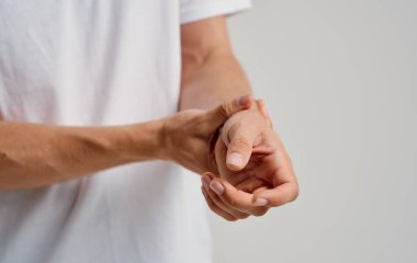 Beyaz tişörtlü bir adam hafif arka planda bileklerine dokunuyor.