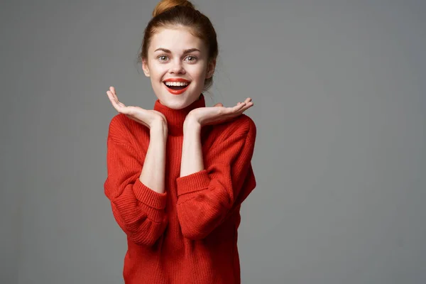 Mujer feliz en un suéter rojo sobre un fondo gris gestos con las manos emociones idea soñar despierto —  Fotos de Stock