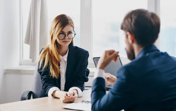 Un hombre de negocios con traje y una mujer se comunican en el trabajo uno frente al otro en la mesa de la oficina — Foto de Stock