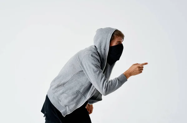 Ladrón hacker masculino en una máscara negra y en una capucha en un robo de fondo ligero — Foto de Stock